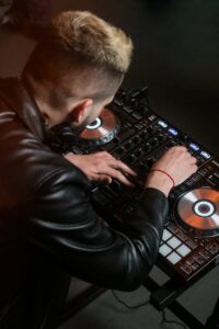 DJ wearing headphones and leather jacket mixing music on a mixer indoors.